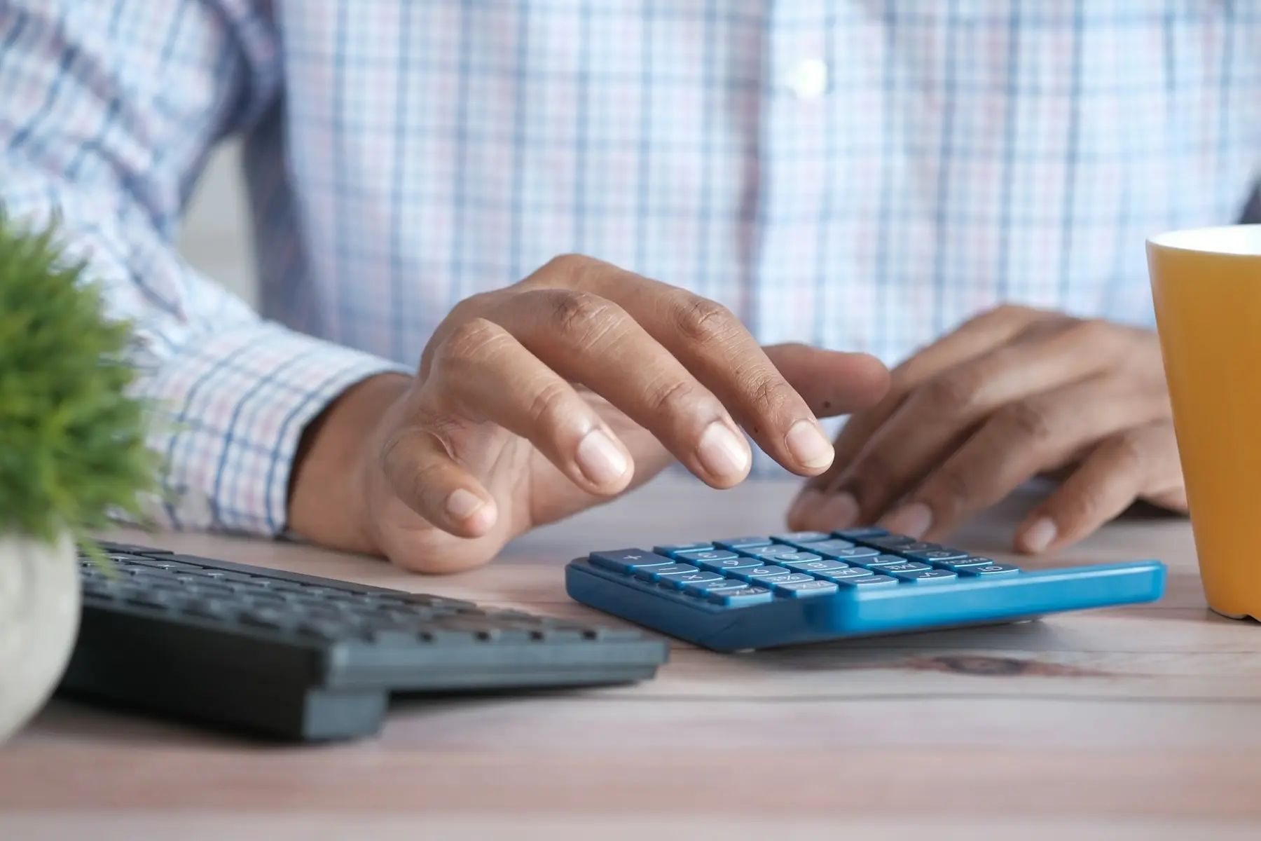 Personne utilisant une calculatrice bleue à côté d’un ordinateur portable.