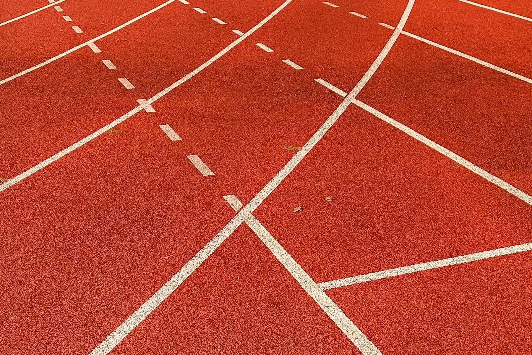 Lignes blanches se croisant sur une piste d’athlétisme rouge.